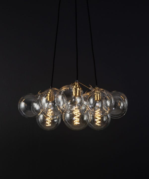 bubble pendant chandelier with 12 clear glass baubles and 3 gold bulb holders suspended from black fabric cable against a black wall