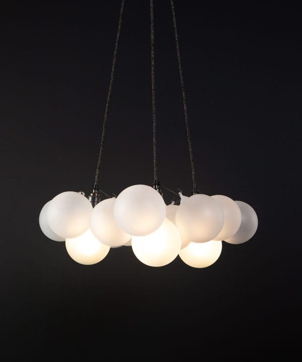 frosted bubble chandelier pendant light featuring 12 frosted baubles and gold bronze holders suspended from black fabric cable against a black wall