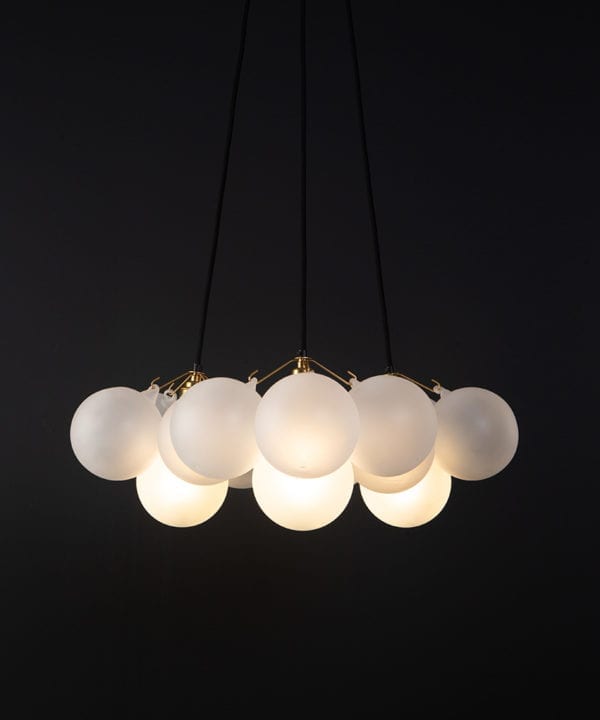 frosted bubble chandelier pendant light featuring 12 frosted baubles and gold bulb holders suspended from black fabric cable against a black wall