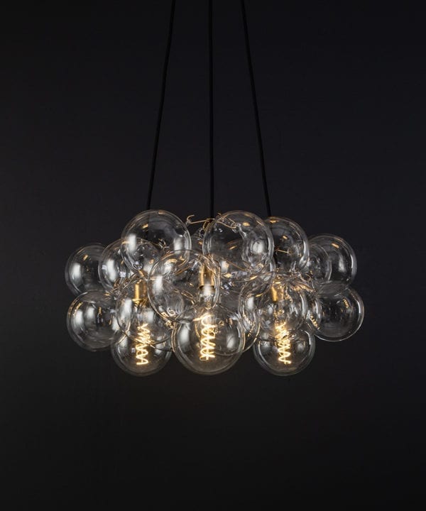 bubble pendant chandelier with 24 clear glass baubles and 3 gold bulb holders suspended from black fabric cable against a black wall