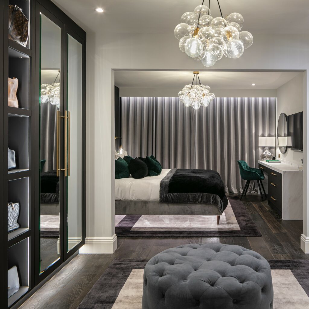 clear medium bubble chandelier suspended above a grey footstool in the dressing roomarea of a grey and white bedroom
