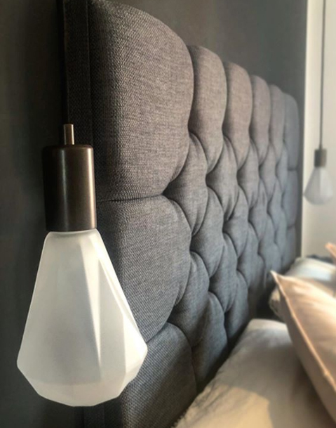 Keren christalle light draped over a grey headboard in a grey and white bedroom