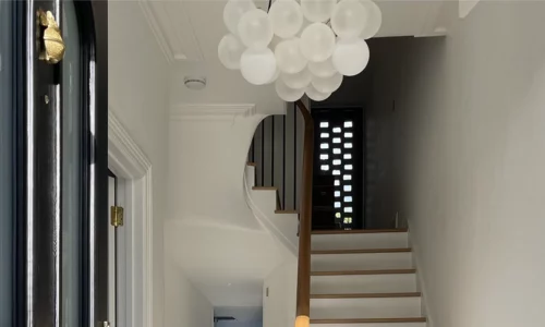 A medium frosted bubble chandelier in a hallway with a black door and a white staircase.