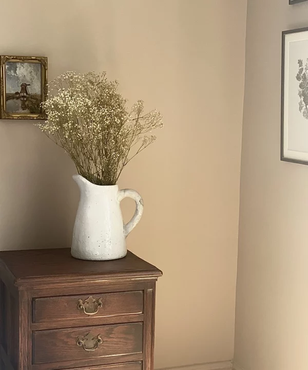 Gypsophila bouquet in a large white jug on top of a dark wood bedside table.