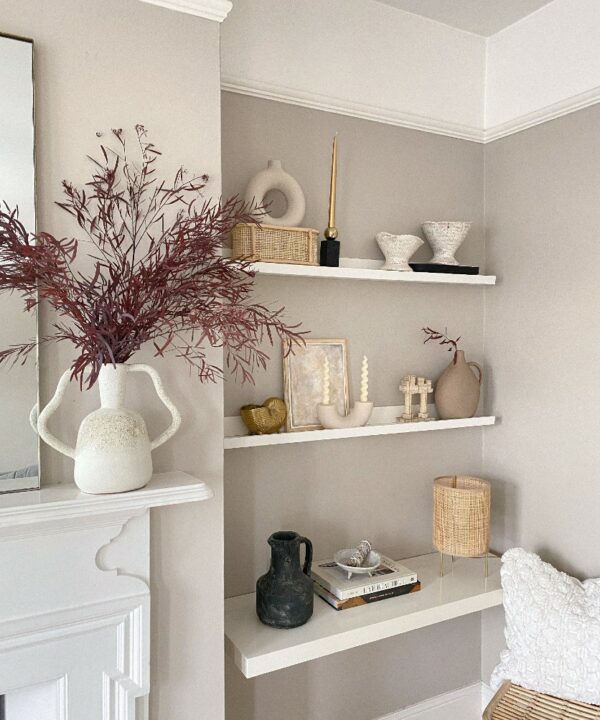 Red eucalyptus nicholii in white vase atop a white fireplace in a neutral living room