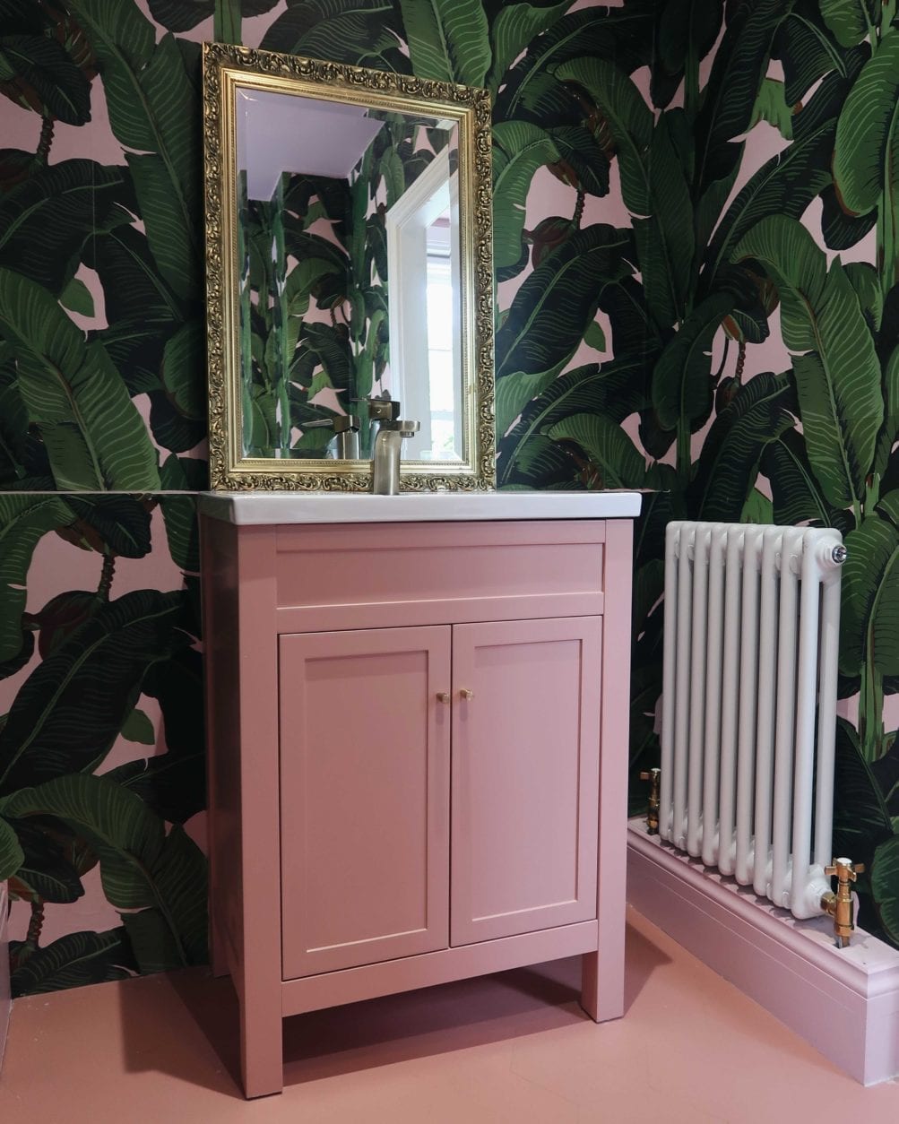 bathroom with pink and green botanical wallpaper, pink under sink cupboard with minimalist brass cupboard handles