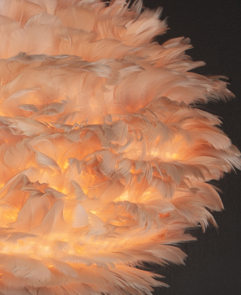 close up image of tripod table lamp with brown feather shade against black background