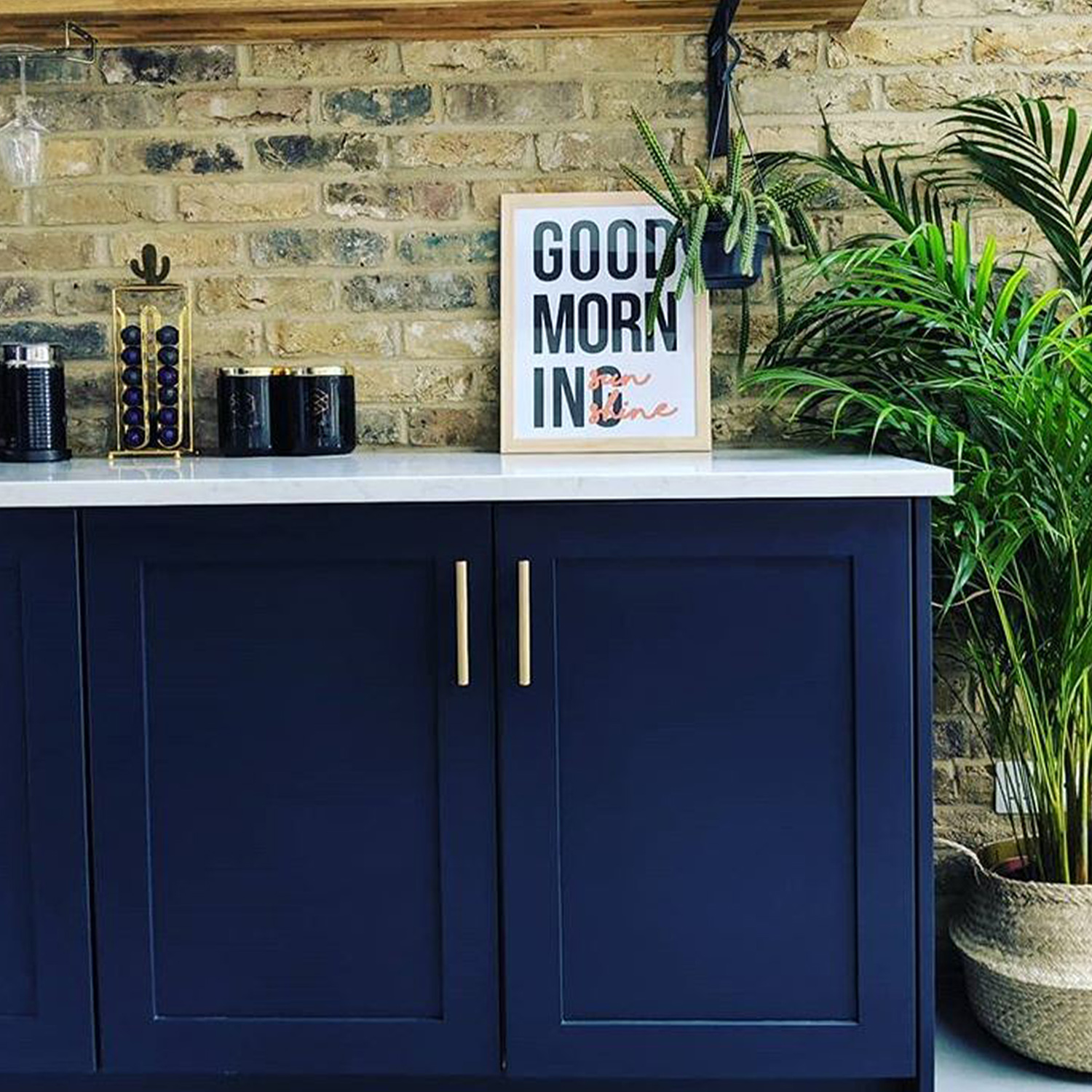 brass skyscraper handles on dark blue cupboards in an exposed brick kitchen