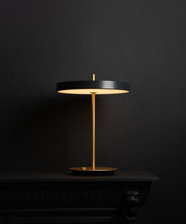 Umage asteria anthracite and brass table lamp with usb charging port on black background switched on