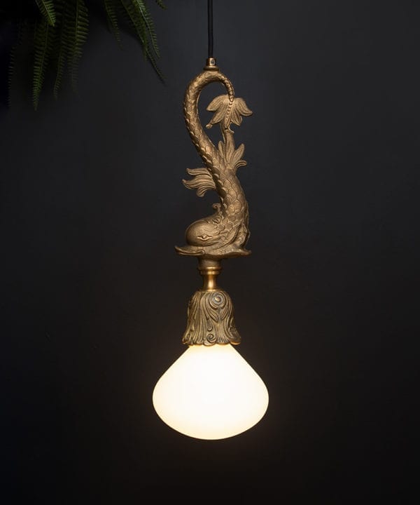 brass pendant fish light with lit bulb suspended from a length of black fabric cable against a black wall