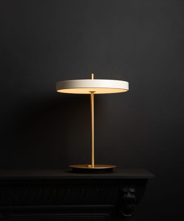 umage asteria pearl white and brass table lamp with usb charging port on black background switched on
