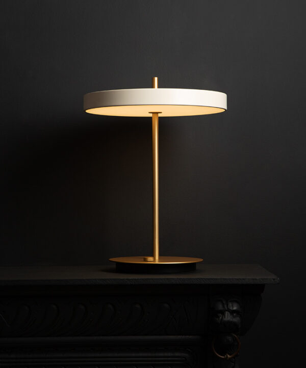 umage asteria pearl white and brass table lamp with usb charging port on black background switched on