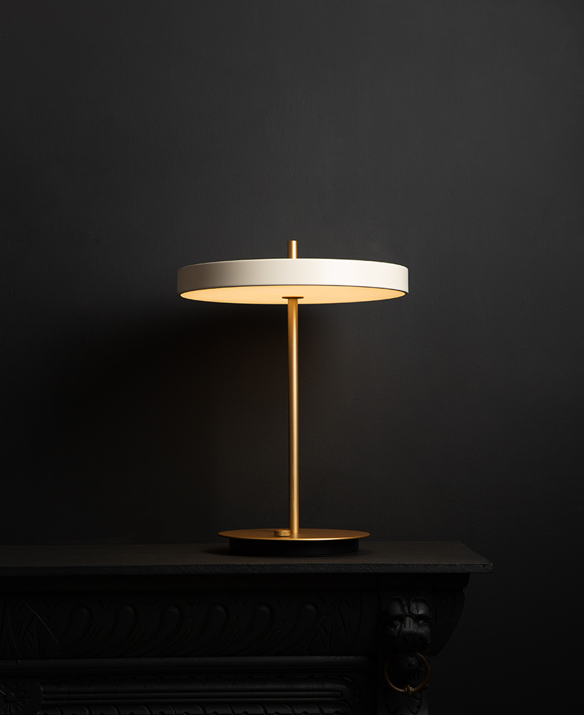 umage asteria pearl white and brass table lamp with usb charging port on black background switched on