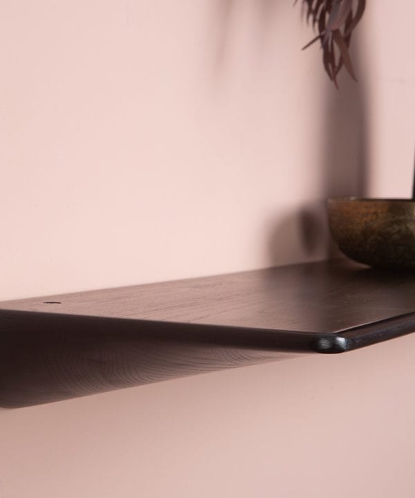 Close up of black floating shelf on a pink wall