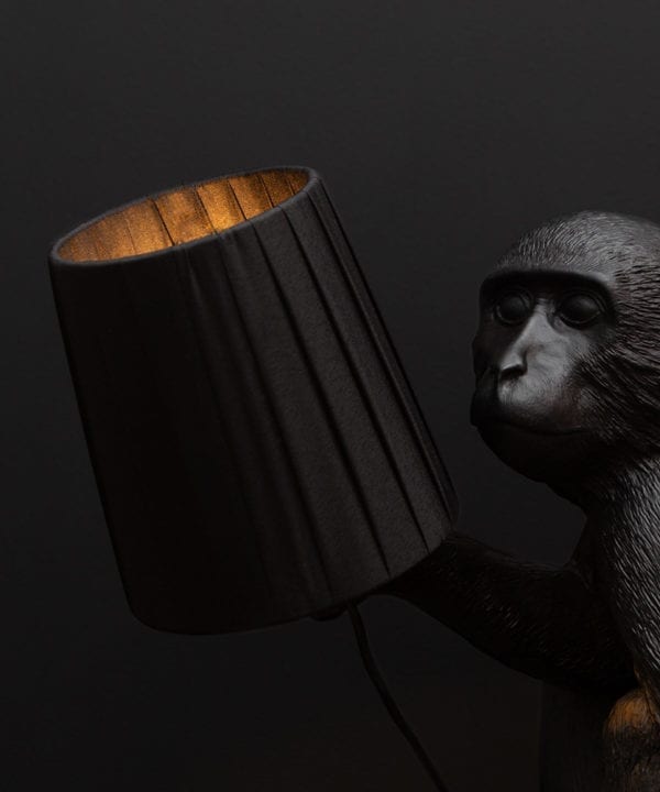 closeup of black lamp shade held in the hand of a monkey table lamp against black background