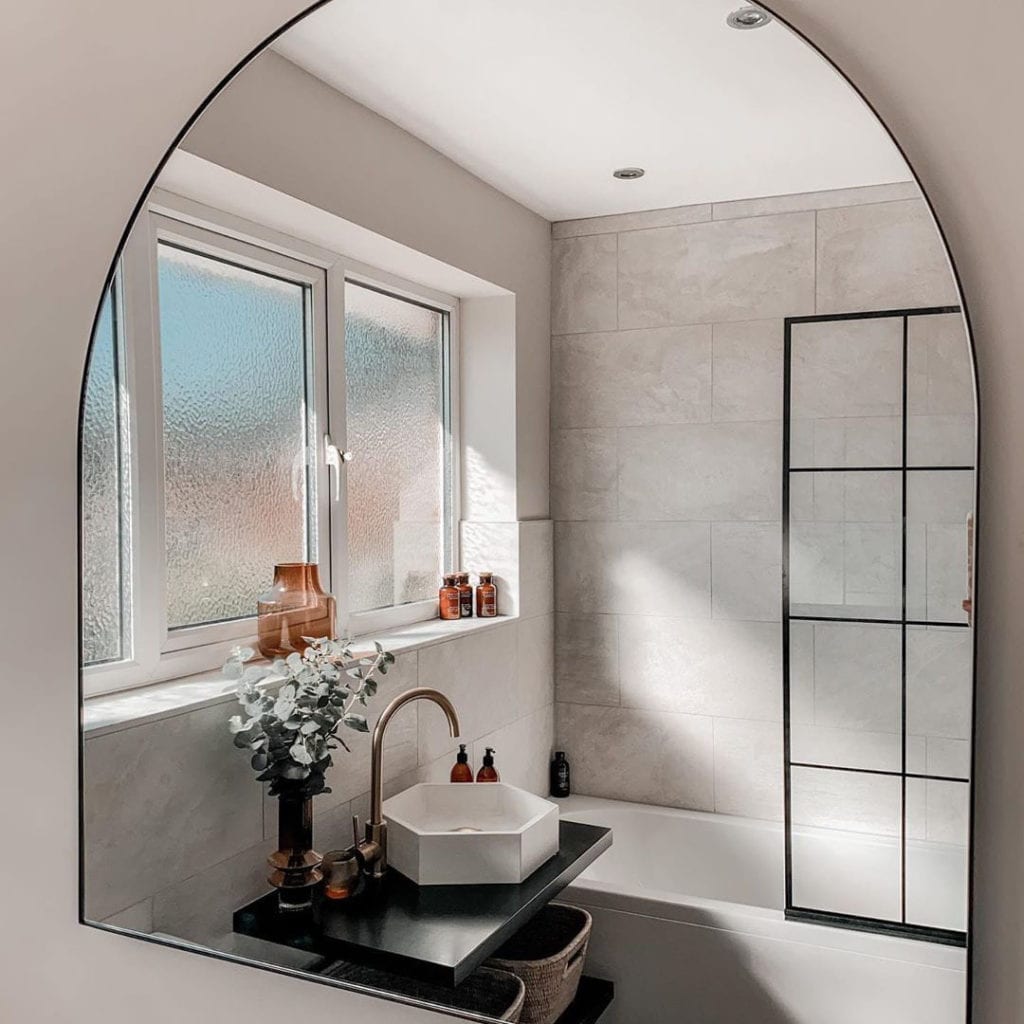 tinkisso gold top sitting next to a hexagonal sink in a white and marble tiled bathroom