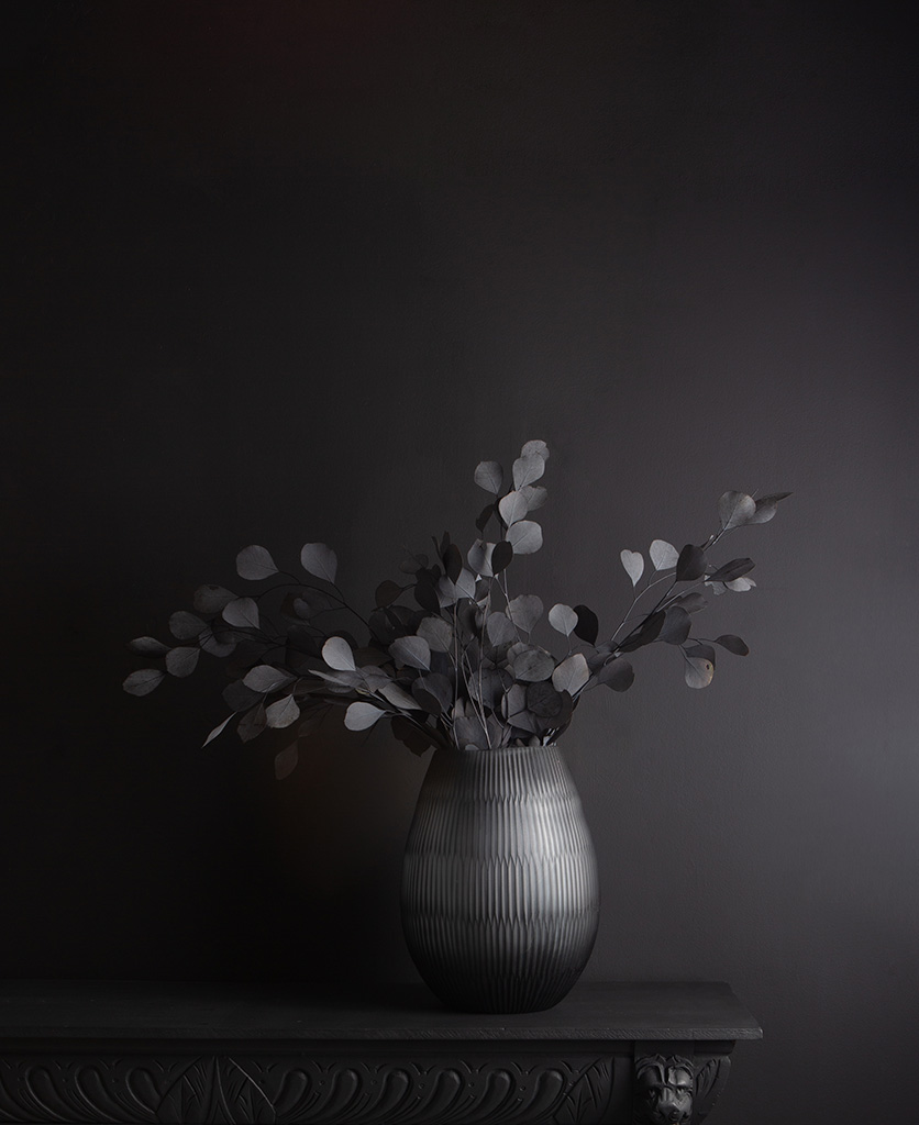 tall glass vase with preserved eucalyptus bouquet against black background