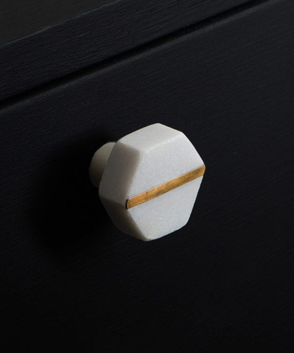 White hexagonal marble knob with brass stripe on black cupboard