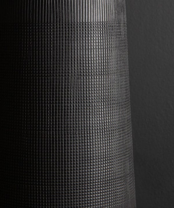 close up of black tall vase against black background