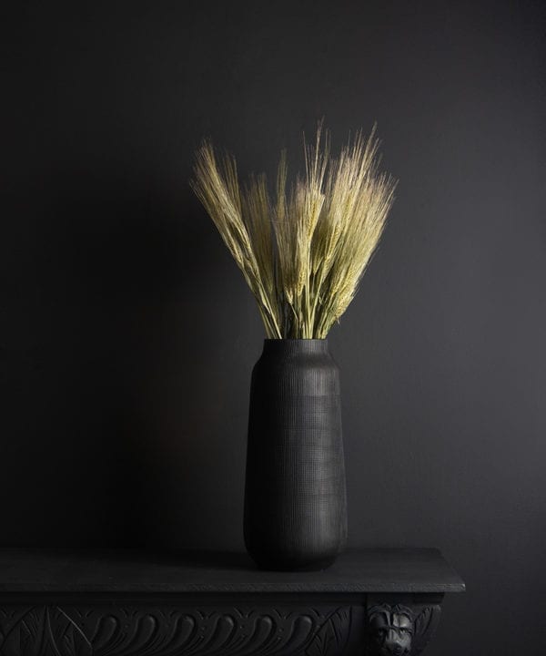 black tall vase with preserved barley bouquet against black background