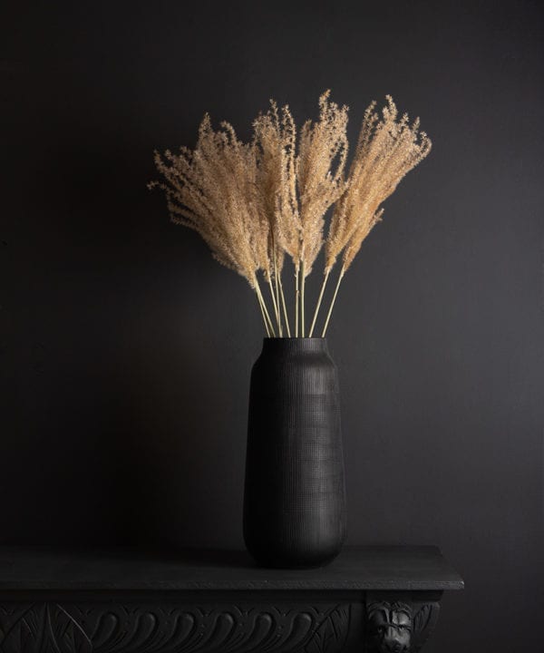 black tall vase with dried fluffy reed grass bouquet against black background