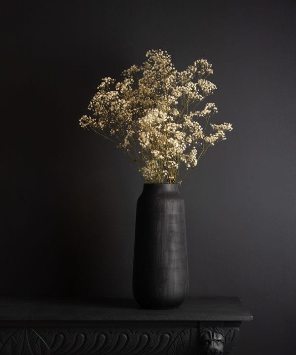 black tall vase with preserved gypsophila bouquet against black background