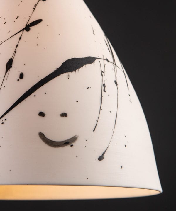 closeup view of painted smiley face on Michael O Hare porcelain light shade against black background