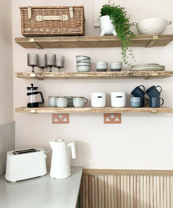 cinnamon and white double sockets installed beneath wooden open shelving in a kitchen