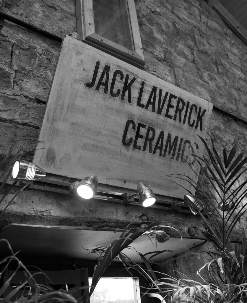 A sign with Jack Lavericks ceramic studio info on against exposed brick wall