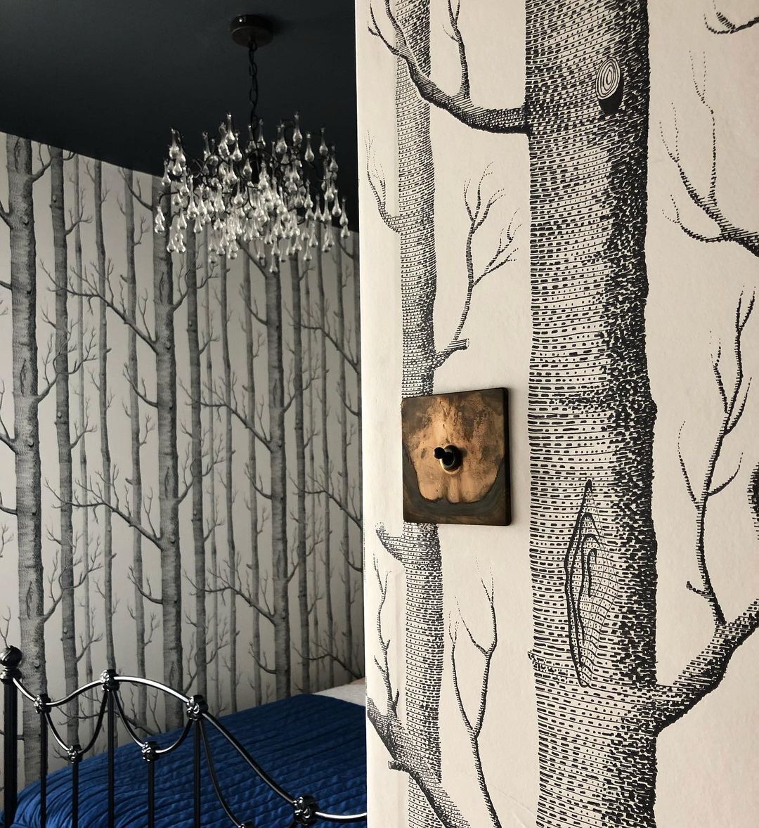 bedroom with white and black tree-print wallpaper with a smoked gold and black single toggle switch on the wall