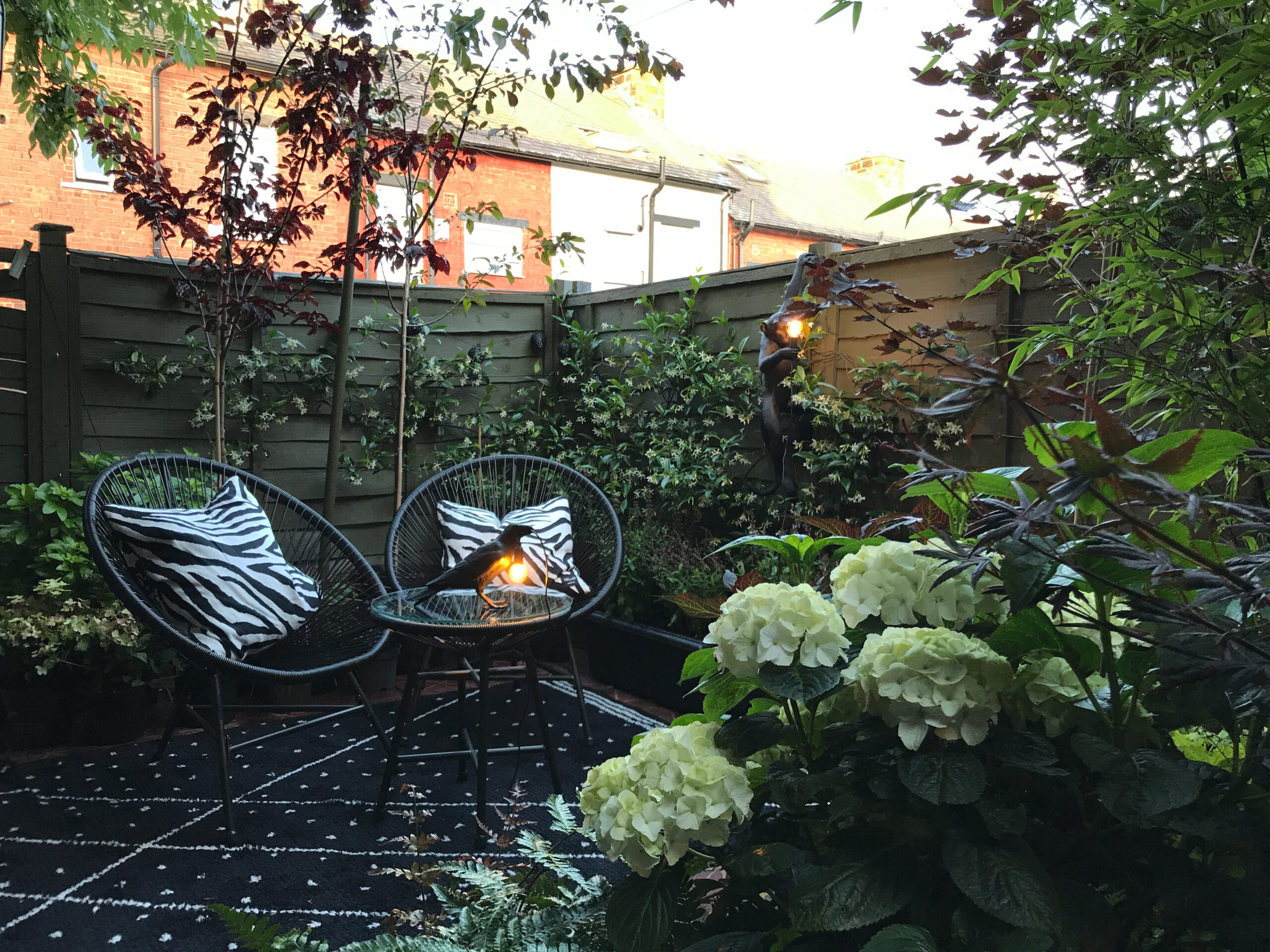 garden patio with two chairs and a table, a black raven table lamp and black monkey wall light