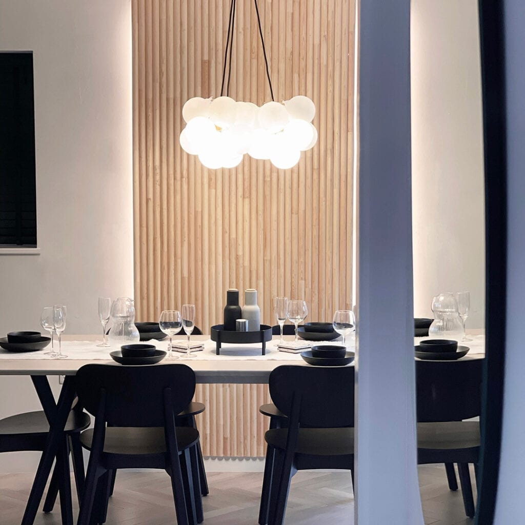 frosted bubble chandelier suspended above a white dining table in front of a wooden cladded wall.