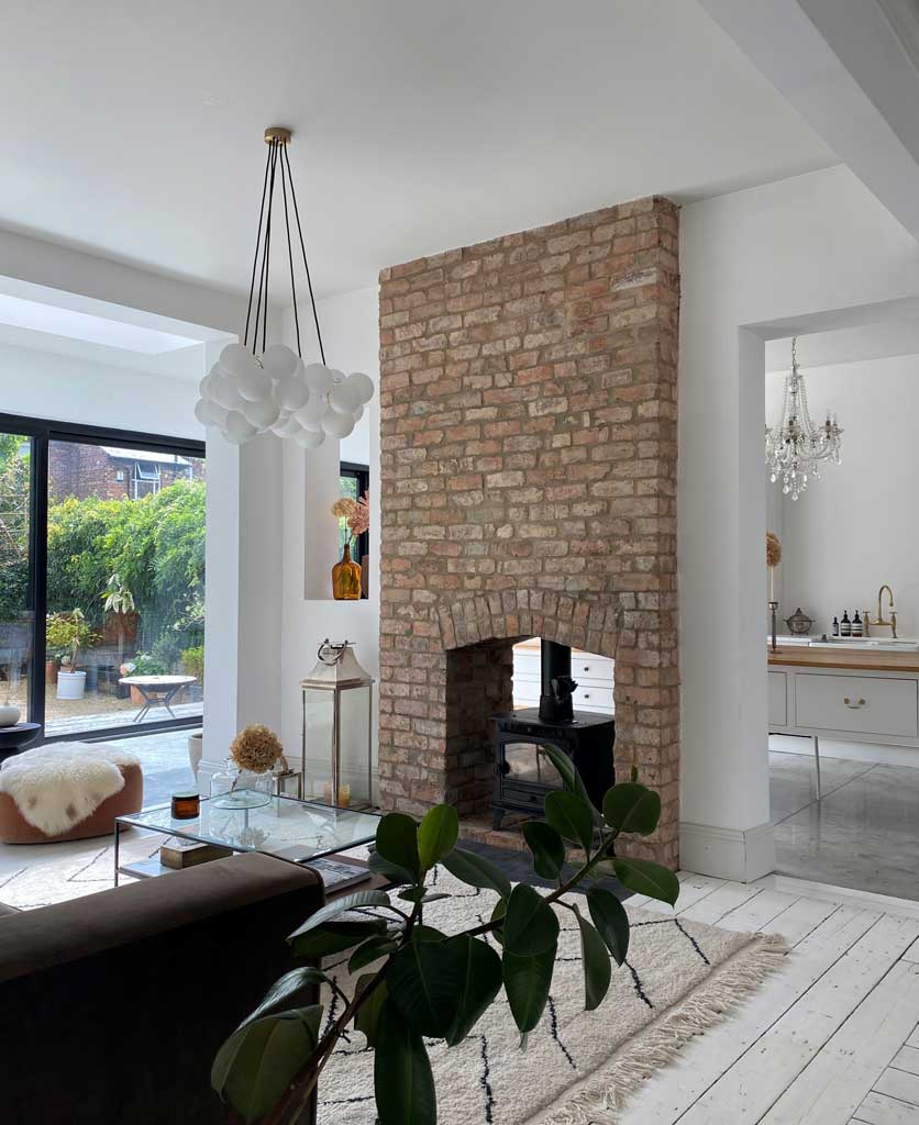 five point frosted bubble chandelier suspended in white living room next to an exposed brick wall with log burner