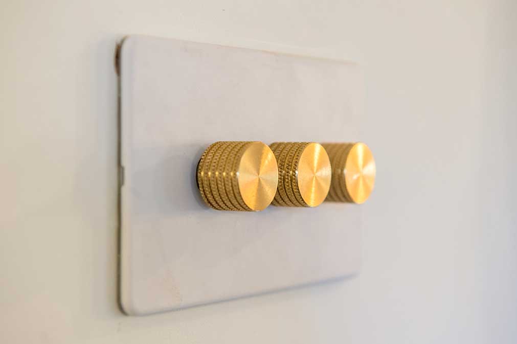 white dimmer switch with three gold knobs against white wall