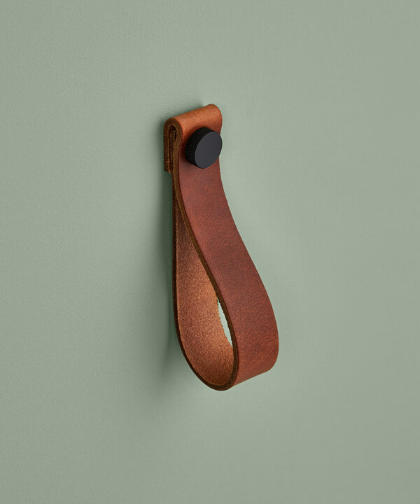 large dark tan magni handle with black stud against sage green background