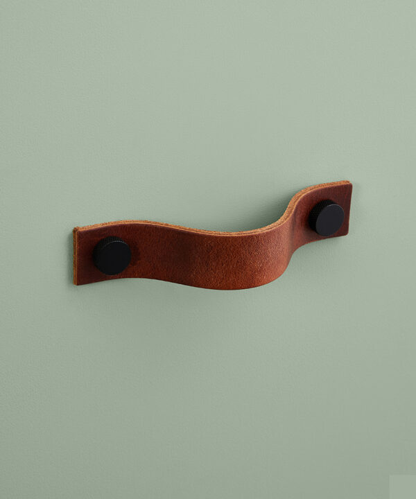 large dark tan Thor leather handle with black knobs against green background