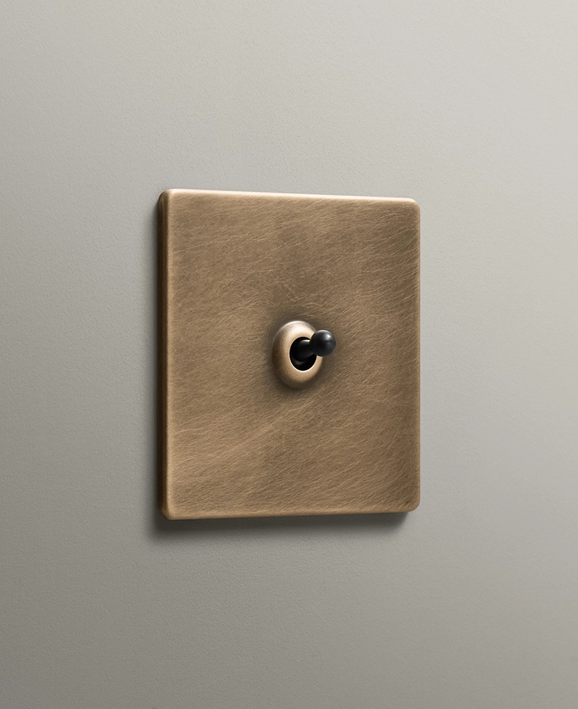 antique brass single toggle light switch on a taupe painted wall