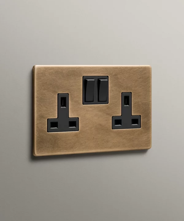 antique brass 2 gang double socket with black inserts on a neutral grey background