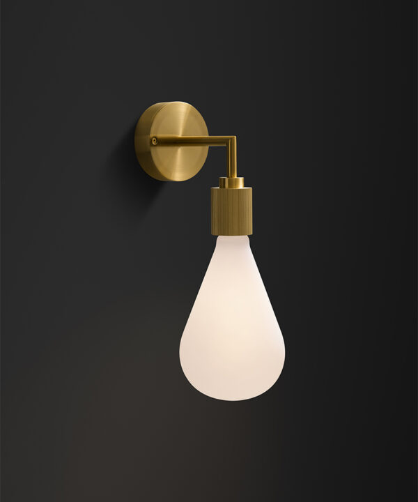 gold art deco wall light with opaque teardrop light bulb on a black painted wall