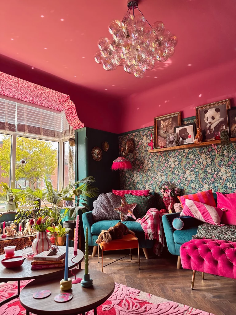 A colourful living room with a dark pink ceiling and an iridescent bubble chandelier and teal floral wallpaper.