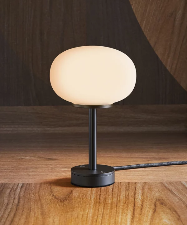 small black table lamp with opaque glass shade shot against a wood effect wallpaper