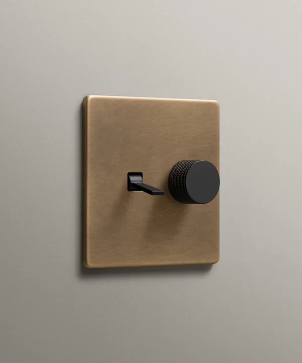 antique brass combination light switch with tapered toggle and knurled dimmer knob in black on a warm neutral background