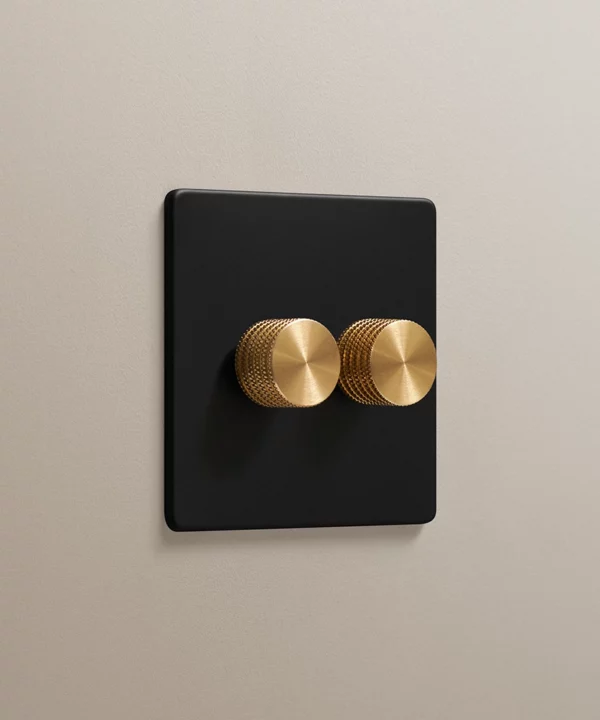 matt black 2 gang double dimmer with knurled dimmer knobs in gold on a neutral taupe painted wall