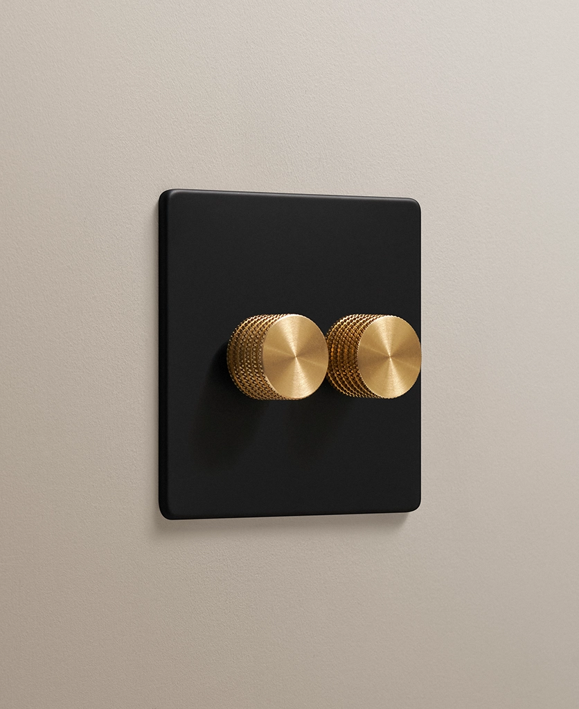 matt black 2 gang double dimmer with knurled dimmer knobs in gold on a neutral taupe painted wall