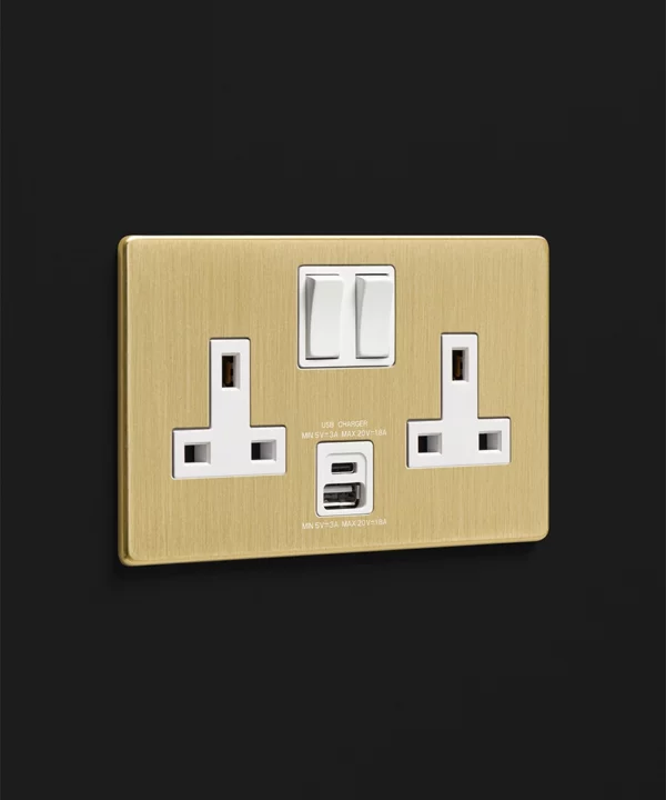 brushed gold USB/USBC double 2 gang socket with white inserts photographed on a black wall