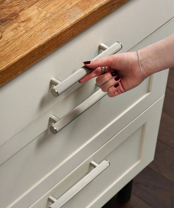 ribbed dull nickel kitchen unit handles on neutral shaker-style drawers with a hand reaching to open