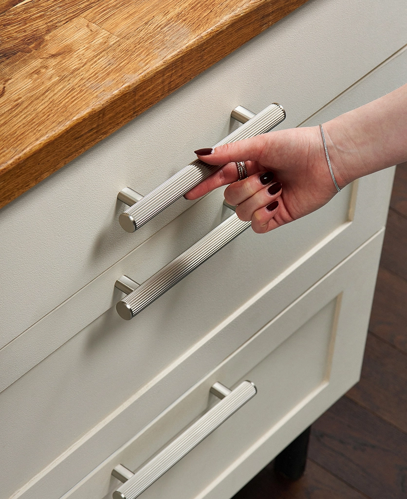 ribbed dull nickel kitchen unit handles on neutral shaker-style drawers with a hand reaching to open