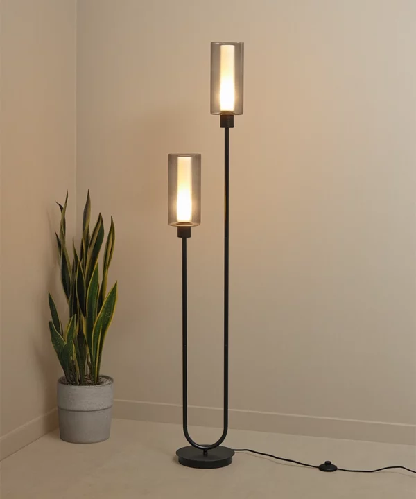 black floor lamp lit with two bulbs within ribbed glass shades on a neutral background with potted plant