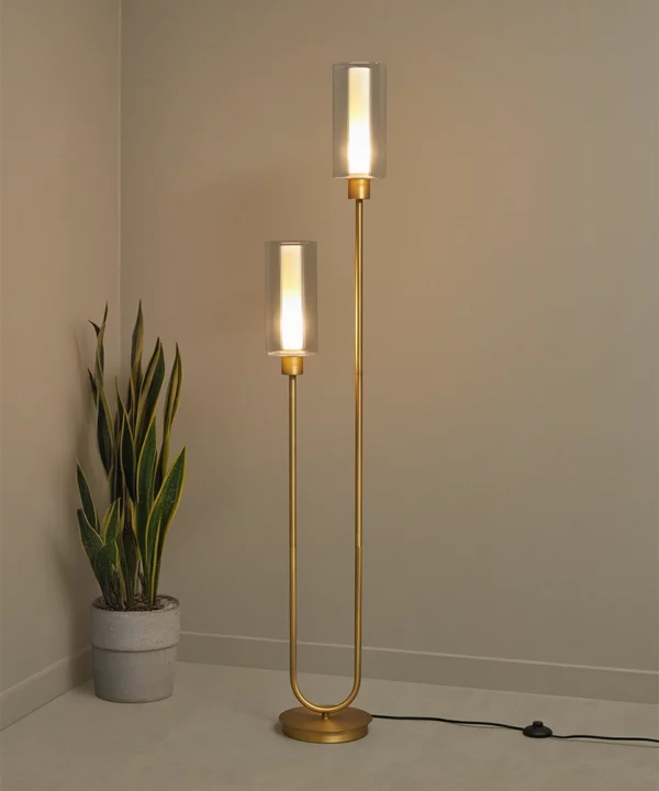 gold floor lamp lit with two bulbs in ribbed glass shades against a neutral background with a potted plant