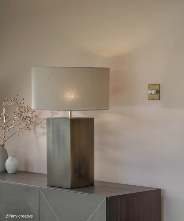 Antique Brass table lamp with rectangular base and neutral shade on a sideboard.